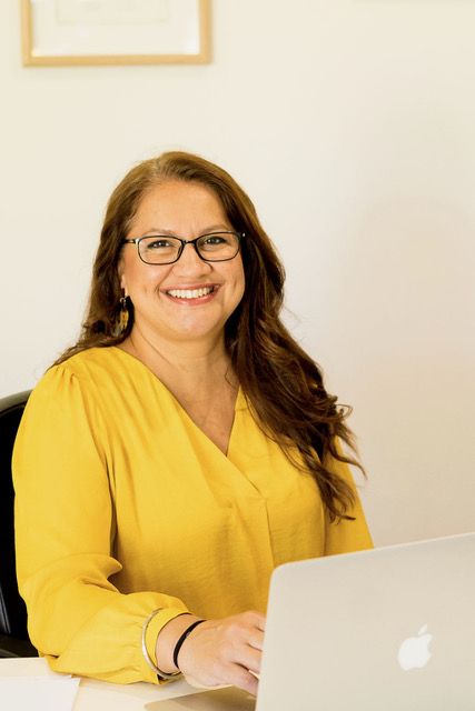 Sim Dhaliwal, speech pathologist and educator, smiling warmly at her desk